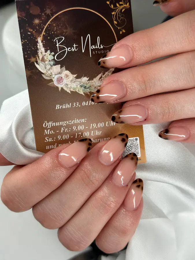 Hand mit Tortoise-French-Nägeln hält die Visitenkarte von Best Nails Studio mit Adresse Brühl 33 und Öffnungszeiten