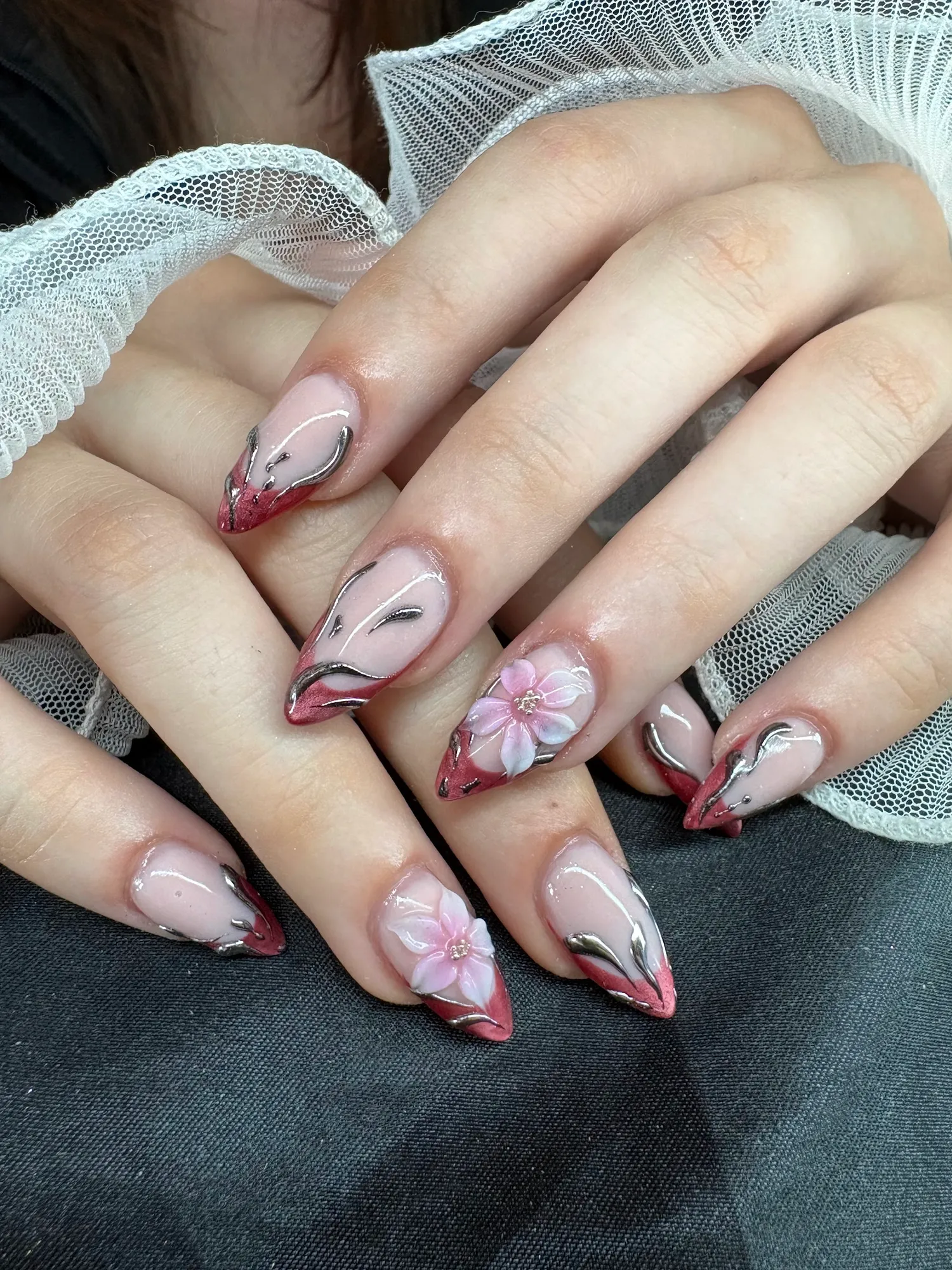 Mandelförmige Nägel mit rosa-rotem Chrome-French, silbernen Linien und 3D-Blüten, auf weißem Tüll