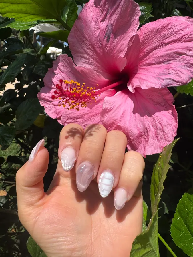 Milchig-weiße Muschel-Nägel vor einer pinken Hibiskusblüte