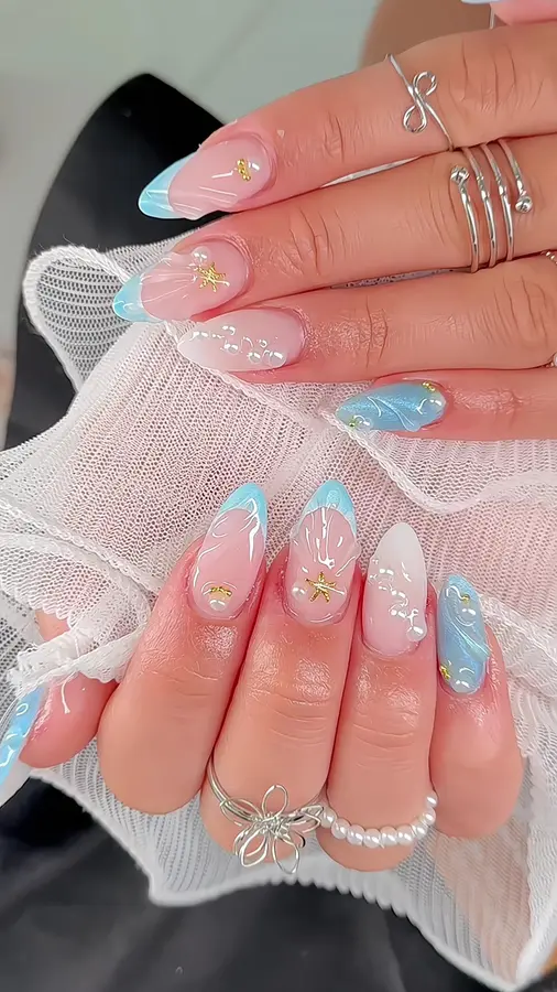 Nail Art in Hellblau und Rosé mit Muschelmotiven, Perlen und goldenen Sternen